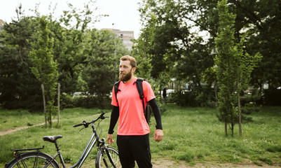  A handsome young guy standing next to his bike in the park