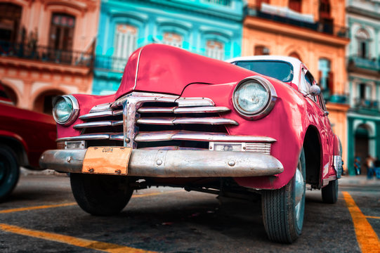 Old car painted hot pink and colorful buildings in Havana