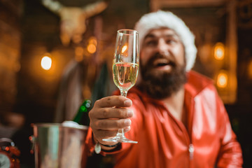 Handsome macho man wearing Santa clothes. Man with beard holds glass of champagne. Holidays.
