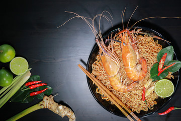 Top view of Spicy instant noodles soup with rivers shrimp on top, on black table background. Tom Yum Kung name in Thailand Foods Style. Dark tone.