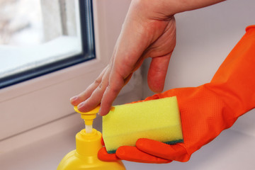 Hands in gloves of orange color and spray for cleaning of windows. Wash glasses. Selective soft focus. Window cleaning at home