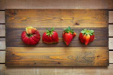 Ugly food. Strange deformed strawberries on wooden background. Misshapen produce, food waste...