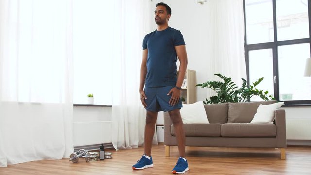 sport and healthy lifestyle concept - indian man with fitness tracker exercising and doing squats at home