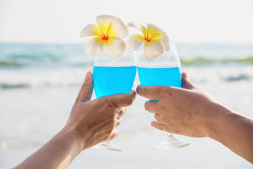 Asian Ccouple holding cocktail glass decoration with plumeria flower with wave sea beach background - happy relax celebration vacation in sea nature concept
