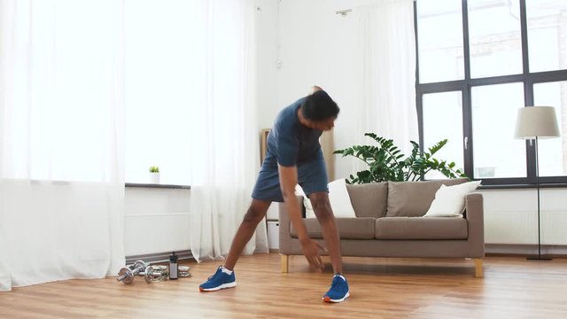 sport and healthy lifestyle concept - indian man with fitness tracker exercising and leaning at home