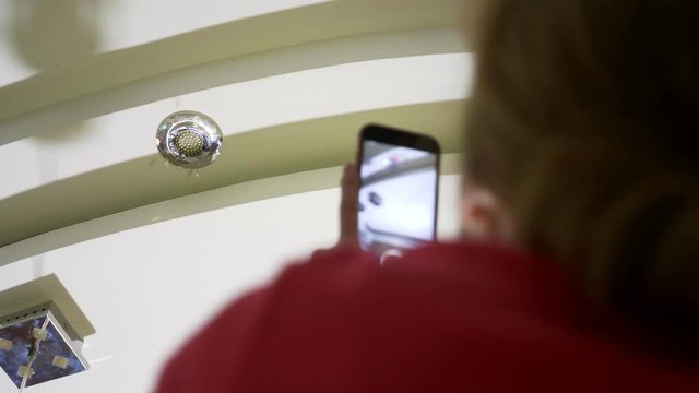 Water damage. concept of flooding the apartment and property insurance. a woman takes a photo on the phone as water drips from the ceiling of her apartment