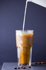 Iced coffee with milk on a dark background. Summer drink with caffeine on the slate board. Latte in a glass cup and coffee beans. Copy space