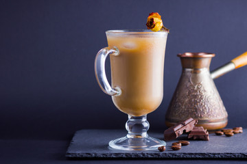 Copper coffee pot (Cezve) and coffee beans. Coffee with milk on dark background. Latte and black chocolate on slate board. Milk drink in glass beaker and dried rose
