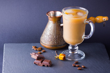 Copper coffee pot (Cezve) and coffee beans. Coffee with milk on dark background. Latte and black chocolate on slate board. Milk drink in glass beaker and dried rose