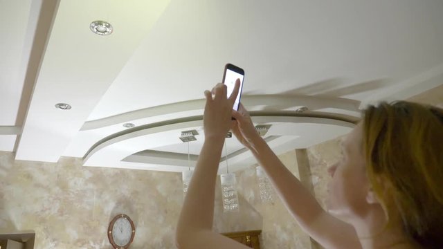Water damage. concept of flooding the apartment and property insurance. a woman takes a photo on the phone as water drips from the ceiling of her apartment