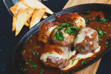 Albondigas de ternera con una salsa pomodoro gratindo con queso en un sarten sobre un fondo negro