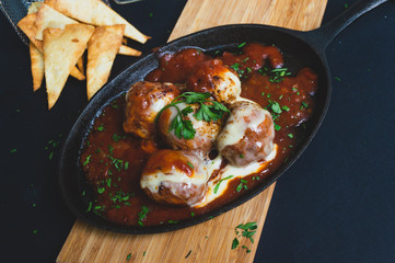 Albondigas de ternera con una salsa pomodoro gratindos con queso emmental  en un sarten sobre un fondo negro vista desde arriba