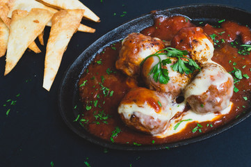 Albondigas de ternera con una salsa pomodoro gratindos con queso emmental  en un sarten sobre un fondo negro