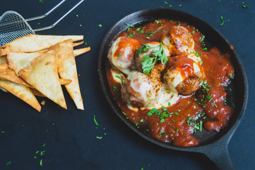 Albondigas de ternera con una salsa pomodoro gratindos con queso emmental  en un sarten sobre un fondo negro