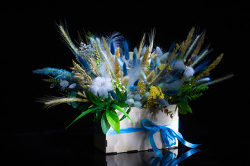 wooden box with beautiful spring floral bouquet decorated with feathers on black background 