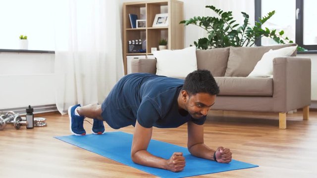 sport, technology and healthy lifestyle concept - indian man using fitness tracker and doing plank exercise at home