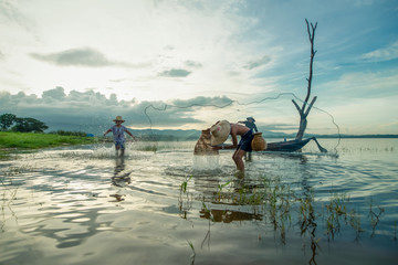 A boy fisherman with catching fish in the early morning. His uncle casting a net for catching fish on wooden boat in neighboring.