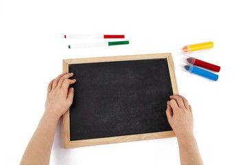 Top view of child hands and empty chalkboard with colorful markers laying around isolated on white