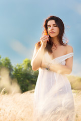 Sexy young happy woman in a cute white summer dress with a flower enjoying the sun standing in a field 