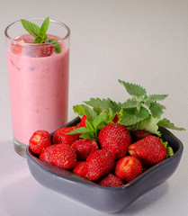 Pink strawberry cocktail decorated with mint leaves near ripe strawberry on white background advertising space
