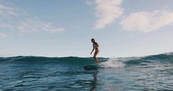 Young woman surfing a wave on her longboard in slow motion, summer surf adventures