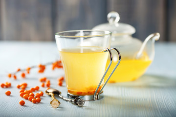 Vitaminic healthy sea buckthorn tea in small glass tea pot with fresh raw sea buckthorn berries. Selective focus