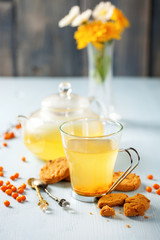 Vitaminic healthy sea buckthorn tea in small glass tea pot with fresh raw sea buckthorn berries. Sea-buckthorn tea and cookies.  Selective focus