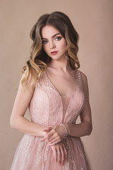 Attractive young girl portrait in evening dress on the beige background