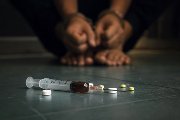 Syringe and drugs with out of focus man sitting on floor and hands locked in handcuffs.drug addicted.International Day against Drug Abuse and Illicit Trafficking - obrazy, fototapety, plakaty