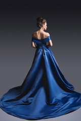 Beautiful woman in elegant blue dress with plume posing on dark background. Back view