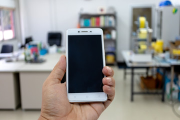 A man hand holding smartphone device in the office background.