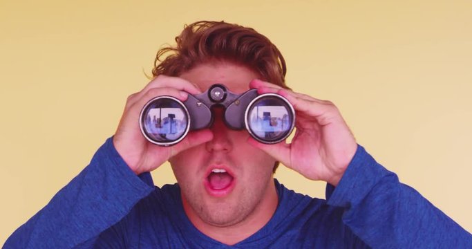 Young funny, surprised man using binoculars to search for something and finding it