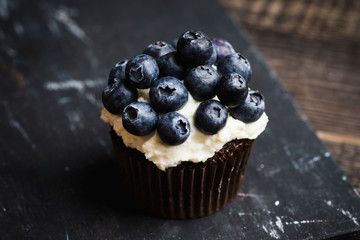 Homemade muffin with blueberry and cream cheese frosting on the rustic background. Selective focus.