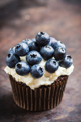 Homemade muffin with blueberry and cream cheese frosting on the rustic background. Selective focus.