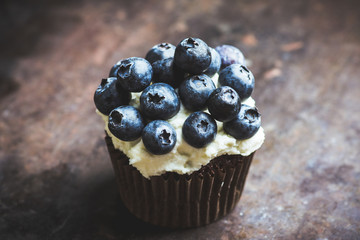 Homemade muffin with blueberry and cream cheese frosting on the rustic background. Selective focus.