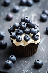 Homemade muffin with blueberry and cream cheese frosting on the rustic background. Selective focus.