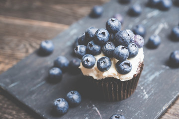 Homemade muffin with blueberry and cream cheese frosting on the rustic background. Selective focus.