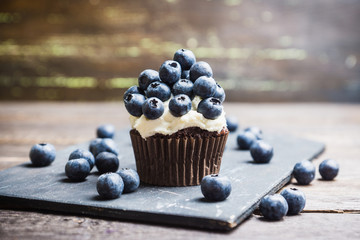 Homemade muffin with blueberry and cream cheese frosting on the rustic background. Selective focus.