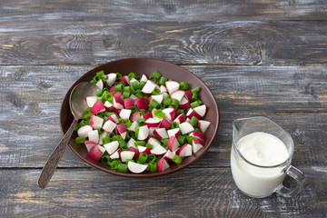 Fresh radish salad with green onions and sour cream on a wooden background, rustic style