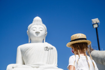 Back view of little girl standing near Big Buddha statue in Phuket, Thailand. Concept of tourism in Asia and famous landmarks