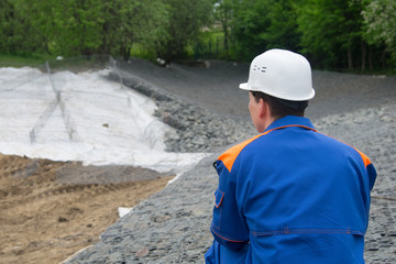 strengthening the shore of the stones the river bed, observation of the worker in blue uniform and white helmet