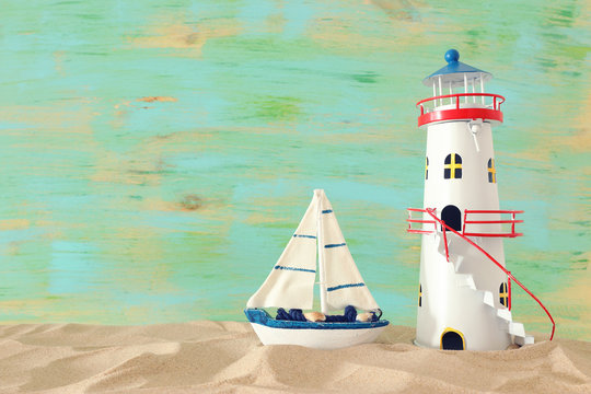 vacation and summer concept with vintage boat, starfish, lighthouse and seashells over beach sand infront of pastel green background