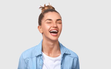 Happy female student with bun hairstyle smiling positively and being in great mood while standing...
