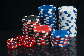 on a black background with reflection, pyramids of multi-colored poker chips and red dice