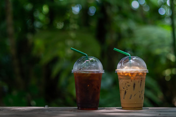 Two  take away plastic cup of iced black coffee americano and iced coffee latte on wood table
