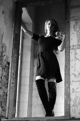 Young beautiful short hair blonde woman in black climbing the stairs, black and white photo. Side view of elegant romantic mysterious lady with movie star look in interior with bricks walls