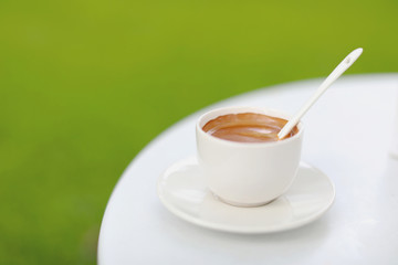White cup of coffee on white table in garden, green background, fresh coffee in garden