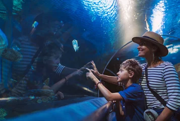 Tuinposter Mother and son walking in indoor huge aquarium tunnel, enjoying a underwater sea inhabitants, showing an interesting to each other. © Soloviova Liudmyla