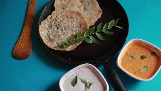 Rotating South Indian food set dosa with curry and chutney on blue background .