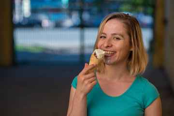 Portrait of a cute girl in a green dress is walking outside and eating dessert. Beautiful blonde enjoying a cone with ice cream on a beautiful summer day. Life is a pleasure